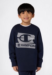 Mørkeblå sweatshirt med et stort hvitt mesh-stil "C"-logo og "CHAMPION" tekst. Laget av et mykt stoff med en avslappet passform og rund hals.