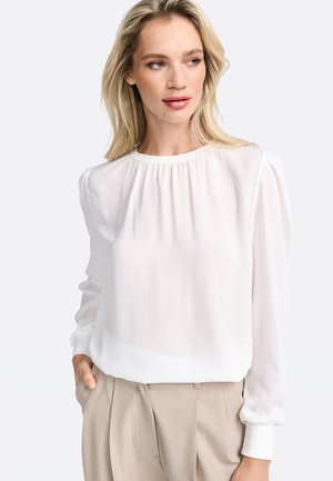 White, long-sleeve blouse with a round neckline and gathered detailing at the shoulders. The fabric appears lightweight and slightly sheer.