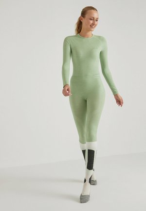 Groene thermische lange mouw top en strakke broek, gemaakt van een geribbeld materiaal. De sokken hebben een wit, zwart en grijs kleurenschema met verticale accenten.