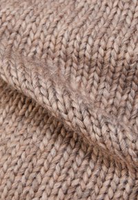 Tissu tricoté en nuances de brun clair, présentant une texture épaisse et rustique avec des fibres visibles et un tissage lâche et superposé.