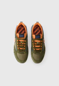 Green sneakers with orange accents, featuring a textured upper, laces, and a padded collar. Branding visible on the tongue and side.