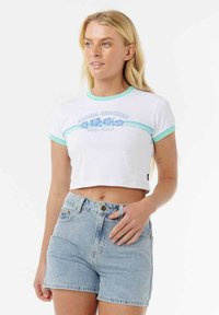 Crop top blanc avec des accents turquoises, arborant un graphisme "Aloha Beaches" et un design floral bleu. Associé à un short en denim clair.