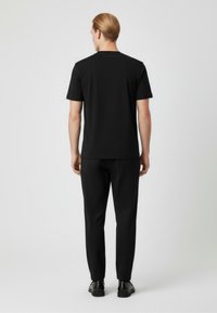 Svart kortärmad skjorta och matchande byxor i slät tyg, med en minimalistisk design och diskret logotyp på baksidan.