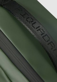 Groene waterdichte rugzak met een gestructureerde afwerking, voorzien van een stevige zwarte band met gedrukt logo en een gladde ritsdetail.