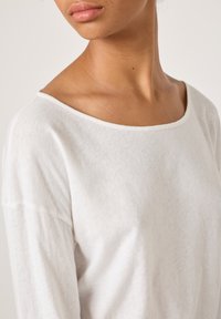 Valge, kerge pika varrukaga särk laia kaelusega, pehme tekstuuriga ja veidi veniv. Kaeluse ääres on nähtavad õmblused.