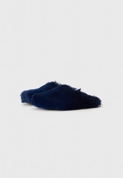 Des chaussons bleus en fausse fourrure à enfiler, de forme arrondie, dotés d'une texture douce et d'un design décontracté, adaptés à un usage intérieur.