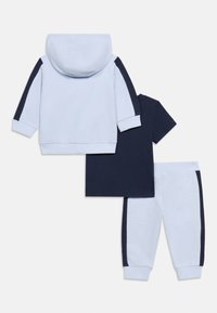 Παιδική φόρμα δίχρωμη με ανοιχτό γαλάζιο φούτερ με κουκούλα και παντελόνι φόρμας με σκούρες μπλε κάθετες ρίγες, συνοδευόμενη από σκούρο μπλε κοντομάνικο μπλουζάκι.