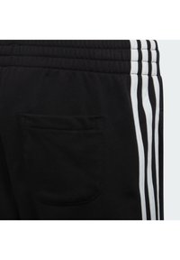 Pantaloni da jogging neri con una tasca posteriore e tre strisce bianche lungo il lato. Realizzati in un tessuto morbido e testurizzato.