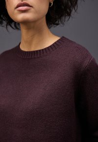 Maglione a maglia viola scuro con collo a girocollo a coste e tessuto testurizzato. La vista ravvicinata mette in evidenza la morbidezza e la lavorazione artigianale.