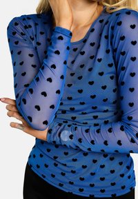 Kék, hosszú ujjú felső áttetsző anyagból, fekete szívmintákkal, kerek nyakkivágással és testhezálló ujjak.