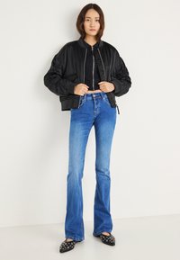 Fekete bomber dzseki puffadt ujjakkal, világoskék bővülő farmerral párosítva. Az öltözéket fekete, kör alakú díszítéssel ellátott hegyes orrú lapos cipők egészítik ki.