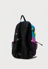 Μαύρο, μπλε και μοβ σακίδιο πλάτης με επενδυμένους ιμάντες ώμων, αγκράφες στο στήθος και τη μέση, και διχτυωτές πλαϊνές θήκες σε απλό φόντο.