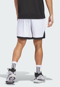 Weiße Sportshorts mit schwarzen Akzenten, kombiniert mit grauen Schuhen und gestreiften Socken. Glatte Textur, knielanges Design und minimale Logodetails.