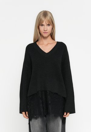 Black knit sweater with a V-neck, loose fit, and long sleeves. Features a textured design and a layered lace hem at the bottom.