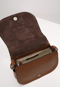 Brun läderhandväska med en texturerad yttersida, slät insida och en ficka med dragkedja. Har en magnetisk stängning och detaljer i guld.