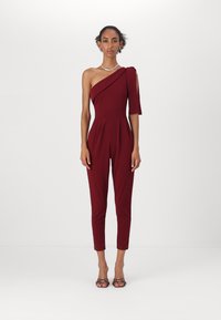 Combinaison bordeaux à une épaule, design ajusté, jambes fuselées, fabriquée dans un tissu lisse, avec un détail de manche latérale et des plis à la taille.