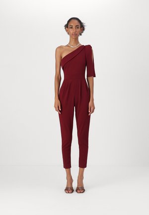 Combinaison bordeaux à une épaule, design ajusté, jambes fuselées, fabriquée dans un tissu lisse, avec un détail de manche latérale et des plis à la taille.