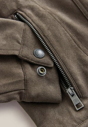 Rjava semiš jakna s srebrnim zadrgo, črnimi gumbi in zlatimi poudarki. Mehka tekstura z natančnim šivanjem in elegantnim dizajnom.