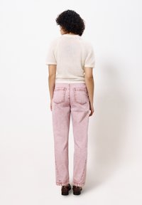 Helle rosa Denim-Jeans mit geradem Schnitt, Fünf-Taschen-Design und Kontrastnähten, kombiniert mit einem cremefarbenen, kurzärmeligen Strickoberteil.