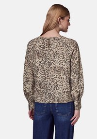 Blouse ample avec un fond beige et un imprimé animal noir. Présente un dos à ouverture en forme de clef et des manches longues. Tissu texturé.