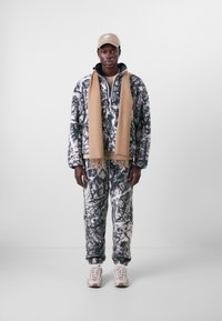 Fleece outfit with black and white marbled pattern, featuring a high collar zip jacket and matching pants; paired with a beige scarf and cap.