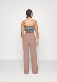 Top floral court avec bretelles spaghetti en noir, vert et violet ; pantalons larges beiges avec une texture douce, présentant une taille haute.
