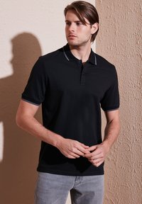 Černé polo tričko s krátkým rukávem, s knoflíkovou légu a kontrastními šedými detaily na límci a zápěstních lemech.