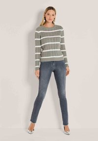 Grauer Kabelstrickpullover mit weißen Streifen, Rundhalsausschnitt und geripptem Saum. Kombiniert mit dunkelblauen Skinny Jeans und silbernen High Heels.