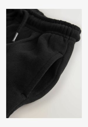 Pantalones jogger de algodón negros con cintura elástica, bolsillos laterales y textura suave. Vista de cerca que destaca el detalle de la tela y las costuras.