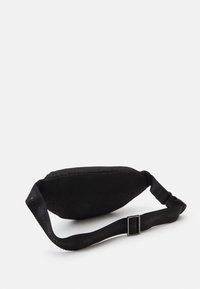 Svart midjeväska med en smidig tygtextur, med ett mönster av logotyper över hela ytan. Justerbar rem med spänne. Rundad form.