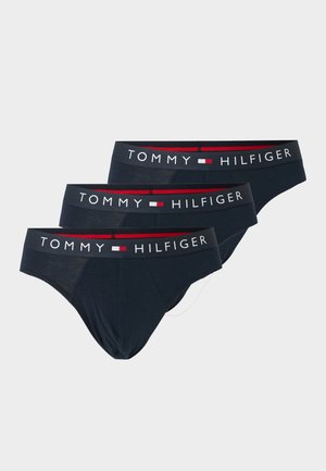 Három fekete férfi alsónadrág, melyeken a „Tommy Hilfiger” márkájú elasztikus derékrész található, a márka piros, fehér és kék logójával.
