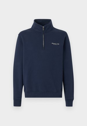 Felpa blu navy con mezza cerniera, polsini e orlo a coste, con piccolo testo bianco ricamato sul petto a sinistra.