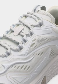 Κοντινή λήψη λευκού αθλητικού παπουτσιού με κορδόνια με σχέδια, πλέγμα και συνθετικές επικαλύψεις, καθώς και υφή στη σόλα.