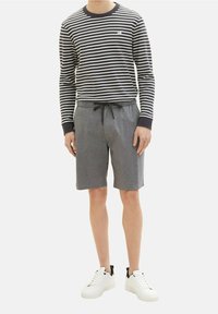 Camicia a maniche lunghe a righe in blu navy e bianco; pantaloni corti grigi con cordoncino e tasche; sneaker bianche con accenti neri.