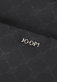 Czarna tkanina z delikatnym tłoczonym wzorem, z wyraźnie widocznymi błyszczącymi złotymi detalami w postaci logo "JOOP!".