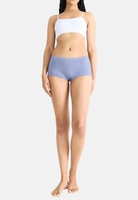 Top corto bianco e mutande hipster blu con motivo circolare e bordo in pizzo, tessuto morbido e design aderente. Modella in piedi a piedi nudi.