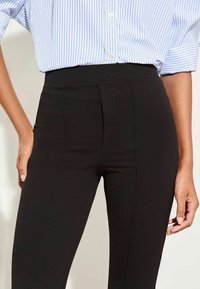 Zwarte high waist broek gemaakt van glad, rekbaar materiaal; heeft een gestroomlijnd ontwerp met een voorkantnaad en een getailleerde pasvorm.