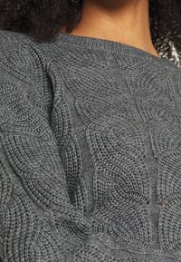 Pull gris tricoté avec un motif texturé présentant des motifs de feuilles en relief. Encolure ronde avec bords côtes. Tissu tricoté doux et épais.