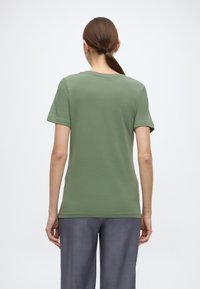 Κοντομάνικο, ελαιδί πράσινο T-shirt από απαλό ύφασμα με άνετη γραμμή· στρογγυλή λαιμόκοψη, απλό σχέδιο, χωρίς εμφανή μοτίβα ή διακοσμήσεις.