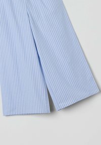 Vaaleansinisiä puuvillapantoja, joissa on valkoisia pystysuoria raitoja. Ne ovat leveälahkeiset ja niissä on siistit, puhtaat helmat, jotka korostavat sileää rakennetta.