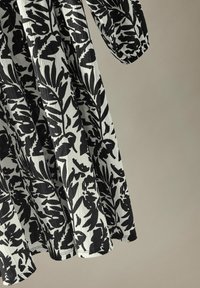 Mustavalkoinen kukkakuosiset mekko, jossa on teksturoitu kangas, pitkät hihat ja virtaava siluetti.
