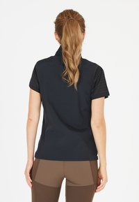Top nero a maniche corte con collo a zip, tessuto liscio e design aderente. La parte posteriore mostra una silhouette elegante e nessun logo visibile.
