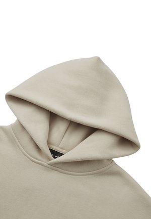 Béžová mikina s veľkou, mäkkou kapucňou, rebrovaným výstrihom a bezšvovým dizajnom. Tkanina pôsobí hladko a jemne elasticky. Vo vnútri je viditeľná štítok s logom.