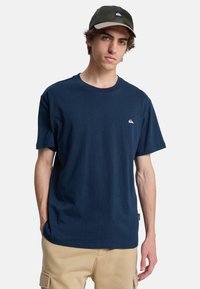 Marineblå bomulds T-shirt med rund hals, korte ærmer og et lille hvidt logo på brystet. Glat tekstur, afslappet pasform.