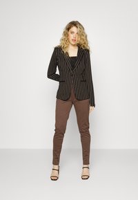 Black and brown striped blazer with a fitted design, paired with brown pants. The outfit features sleek lines and a tailored silhouette.