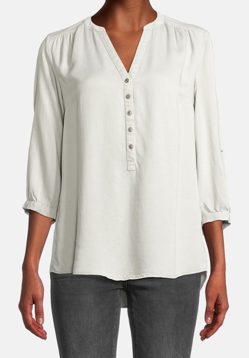 Blusa grigia chiaro a maniche lunghe con scollatura a V e pattina con bottoni. Presenta spalle arricciate e polsini arrotolati, realizzata in un tessuto morbido e liscio.