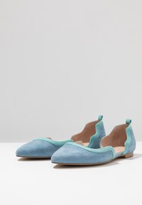 Zamszowe baleriny w jasnoniebieskim i turkusowym kolorze, z ostrym palcem i falistymi wycięciami po bokach. Minimalistyczny design z płaską podeszwą.