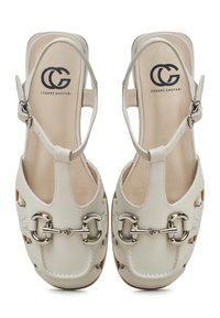 Sandalias de cuero blanco con punta redonda, diseño recortado, acentos en hardware plateado y una correa ajustable en el tobillo. Logo impreso en la plantilla.