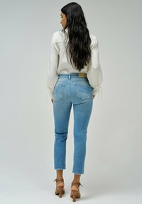 Jeans de tiro alto en un tono azul claro con una silueta ajustada, que cuentan con dos bolsillos traseros y un ligero desgastado, combinados con una blusa blanca texturizada.