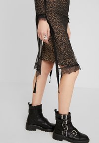 Svart genomskinlig klänning med leopardmönster på insidan, spetsdetaljer vid fållen och svarta band. I kombination med svarta ankelskots med silverdetaljer.